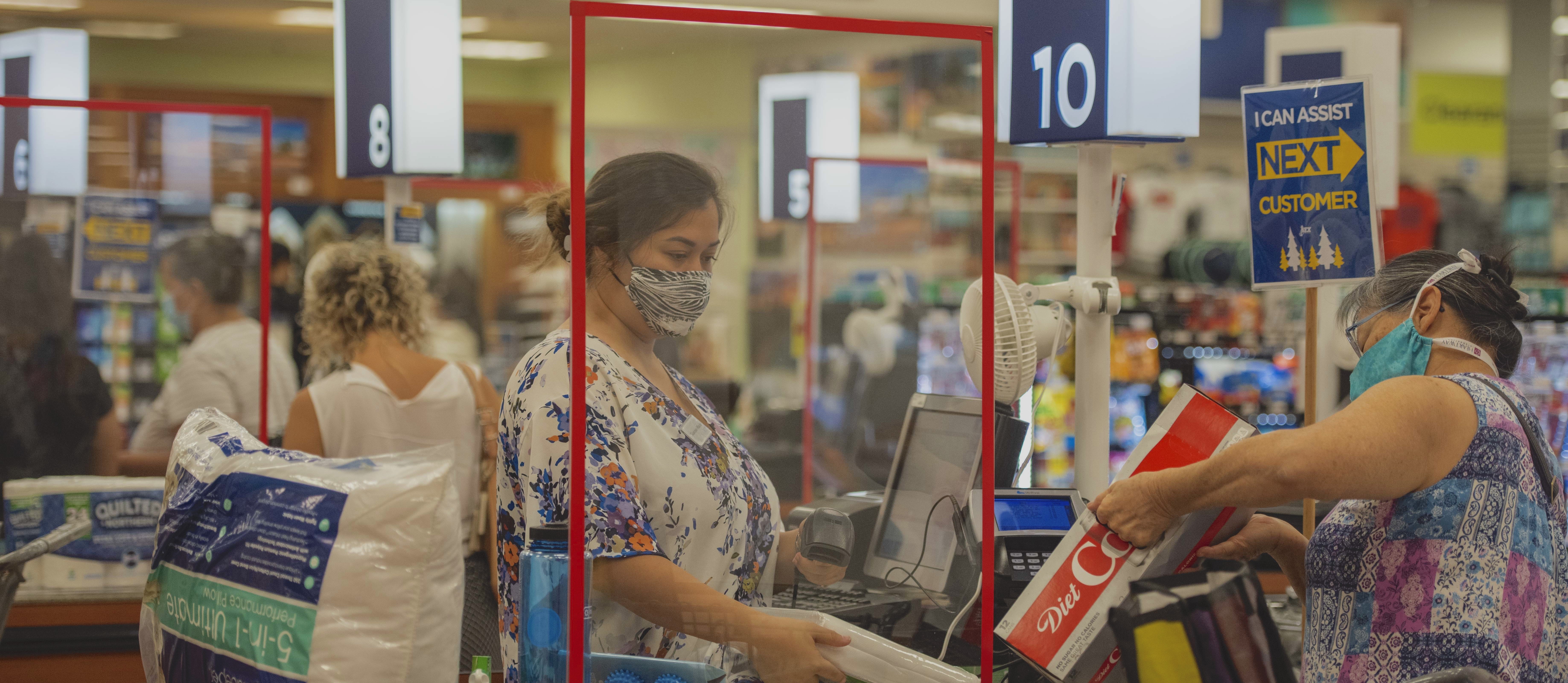 Grocery store check out counter, worker scanning groceries while wearing a mask